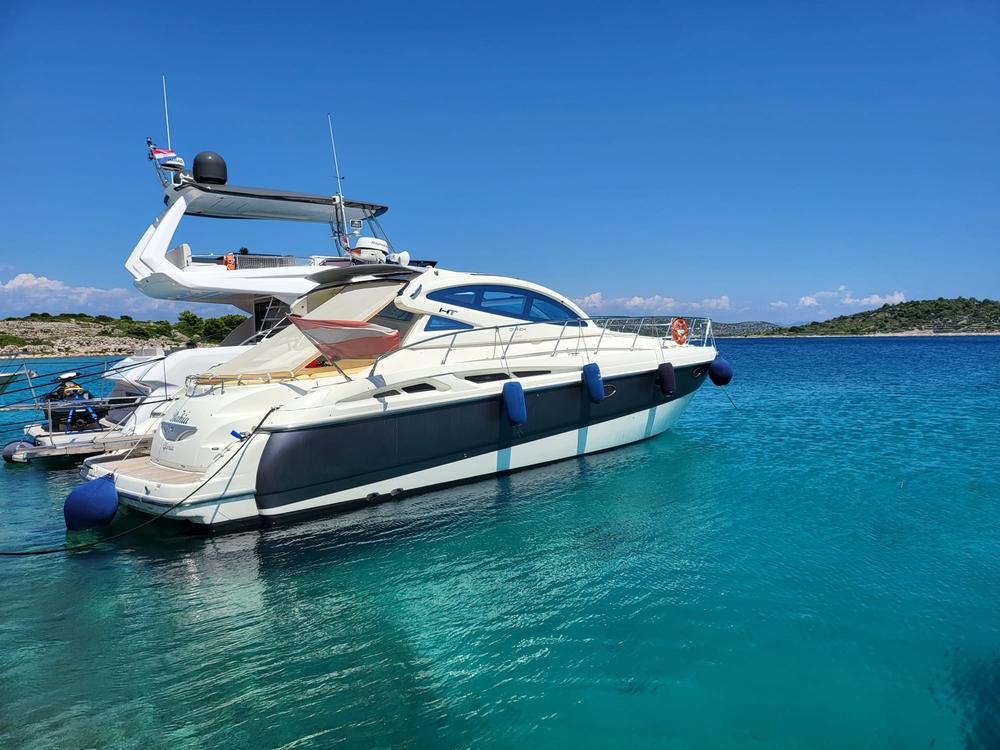 Die Bahia Gloria, eine Cranchi 50 HT mit dunkelblauem Rumpf, vor Anker im türkisen Wasser der Kornaten
