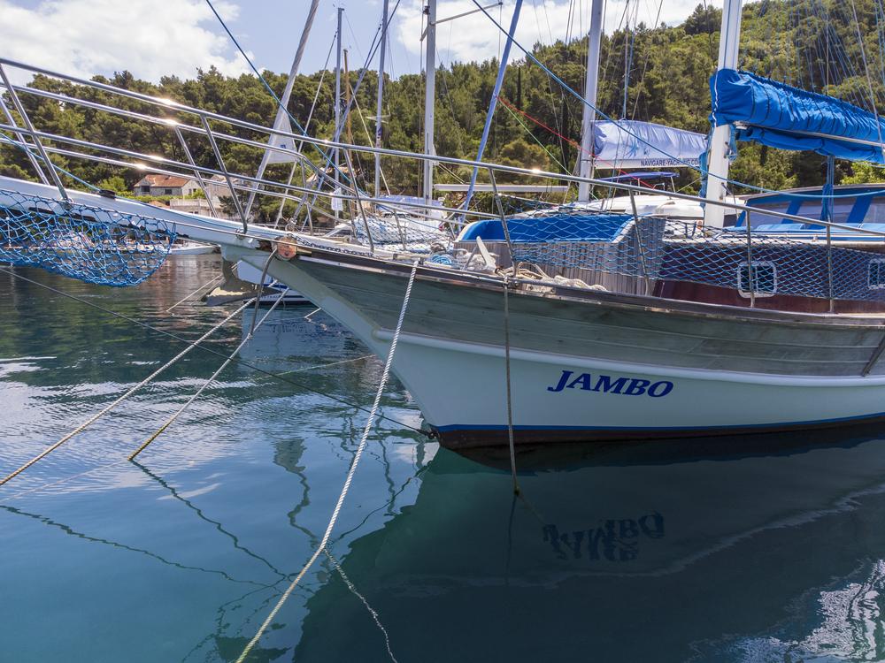 Der Bug des Holzschiffs Jambo mit Schriftzug, gespiegelt im türkisen Wasser