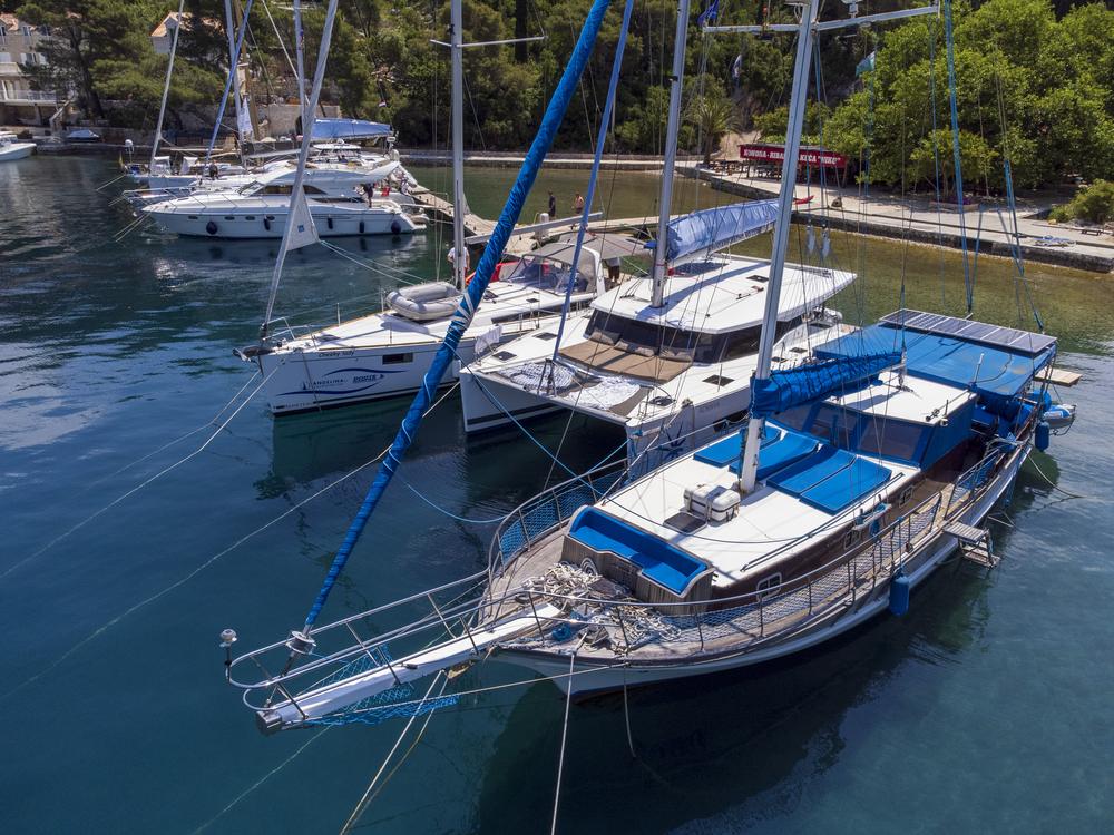 Luftaufnahme von Motoryacht, Katamaran und Holzschiff an einem Steg im türkisen Wasser